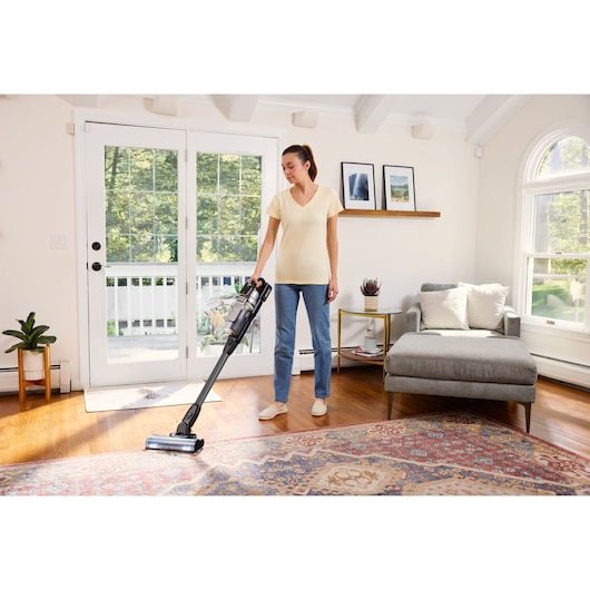 Photo of BLACKDECKER BSV520BL2P cordless stick vacuum in use on hardwood floor near rug in bright living room.