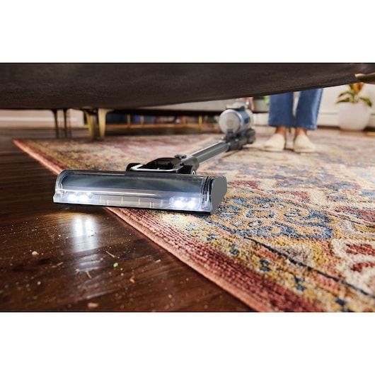 BLACKDECKER BSV520BL2P cordless vacuum cleaning under a sofa on a patterned rug, close-up angle.