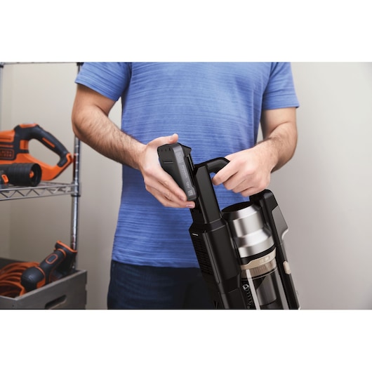 Photo of BLACKDECKER BSV520BL2P cordless vacuum cleaner with person inserting battery, shown from the side indoors.