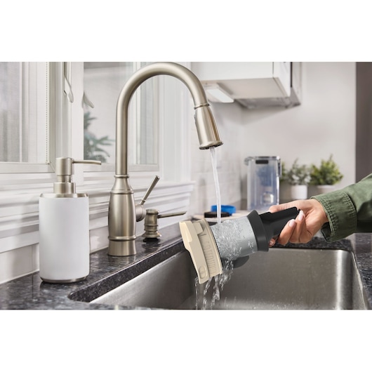 BLACKDECKER BSV520BL2P vacuum filter being rinsed under a kitchen faucet in a modern sink.