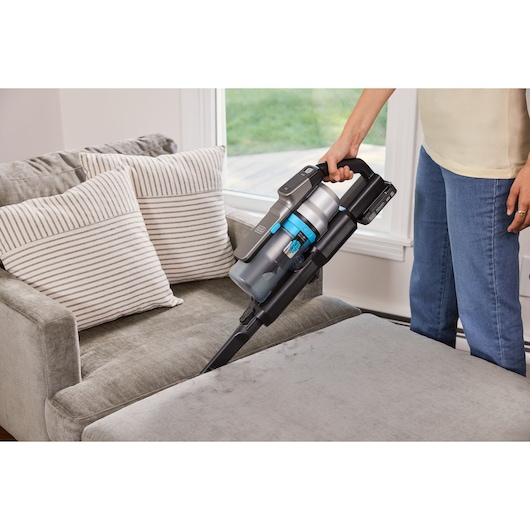 BLACKDECKER BSV520BRB vacuum cleaning gray sofa with striped pillows in living room.