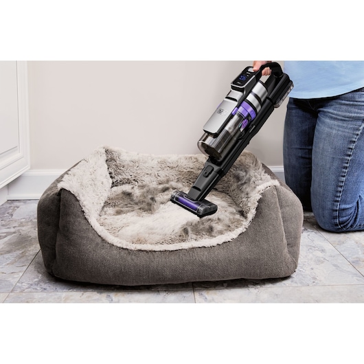 BLACKDECKER BSV520BRP handheld vacuum cleaning a gray plush pet bed on tiled floor.