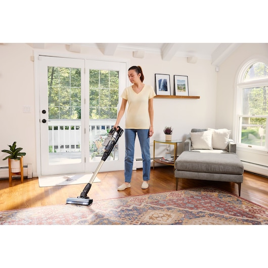 BLACKDECKER BSV525BLP cordless stick vacuum in use on hardwood and rug in bright living room.