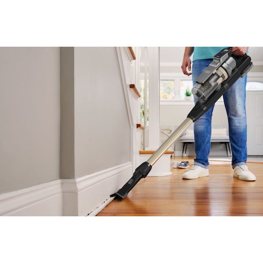 BLACKDECKER BSV525BLP cordless stick vacuum with long extension cleaning baseboards in a modern living room.