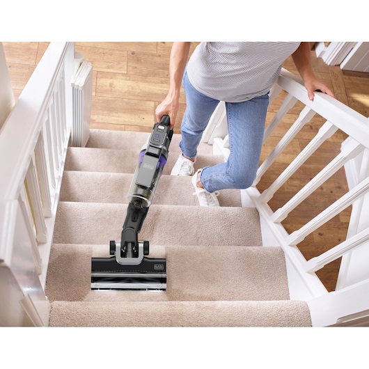 BLACKDECKER BSV525BRP cordless vacuum cleaner cleaning beige carpeted stairs, handheld by a person.