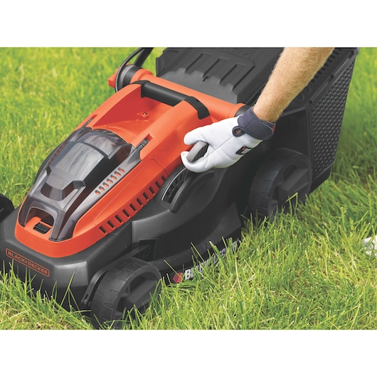 BLACKDECKER CLM3820L1 lawn mower in orange and black, side angle, shown on grass with a gloved hand adjusting lever.