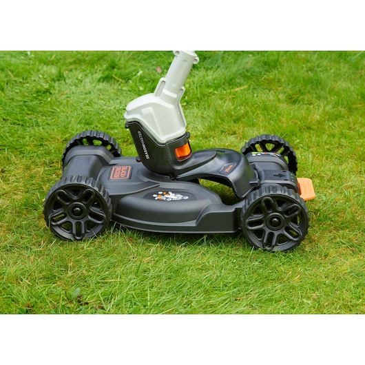 BLACK+DECKER CM100 lawn mower accessory with four black wheels and black body, photographed on green grass.