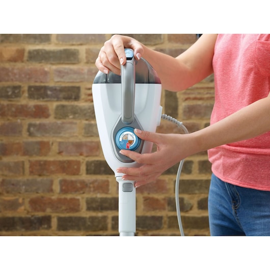 BLACKDECKER FSMH1300FX steam cleaner being adjusted by a person, close-up photo with brick wall background.