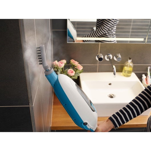 BLACKDECKER FSMH13E10 steam cleaner used on tiled wall in bathroom, close-up angle, flowers and sink visible.