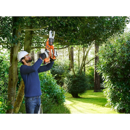 Photo of person using BLACKDECKER GKC1000L cordless pruning saw on tree branches in a garden.