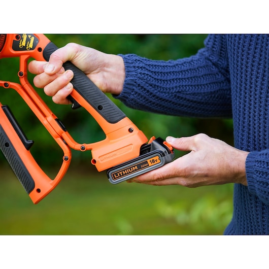 Photo of BLACKDECKER GKC1000L cordless pruner with 18V lithium battery held by a person outdoors.