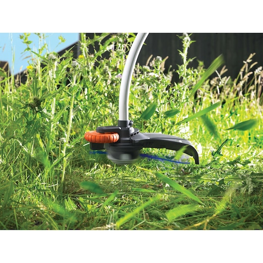 Close-up of a BLACK+DECKER grass trimmer cutting tall grass and weeds outdoors.