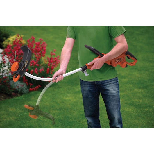 Photo of BLACKDECKER GL7033 grass trimmer in use, orange and black cordless tool, person adjusting handle outdoors.