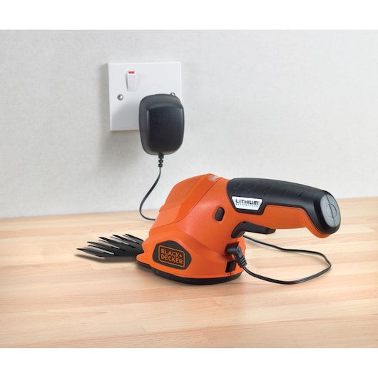 Photo of BLACK+DECKER GSL200 cordless grass shear with charger plugged into wall, side view on wooden surface.