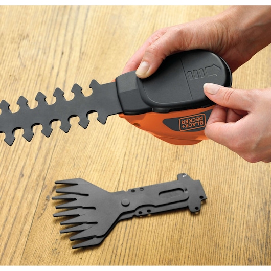 BLACK+DECKER GSL700 handheld shrub shear with black blade, close-up of tool changing blade on wood surface.
