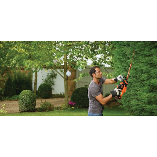 BLACKDECKER GTC18502PC hedge trimmer in use outdoors, orange and black design, trimming tall green hedge