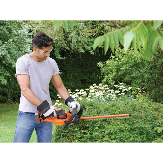 BLACKDECKER GTC18504PC hedge trimmer used outdoors on bushes, orange and black design, battery powered.