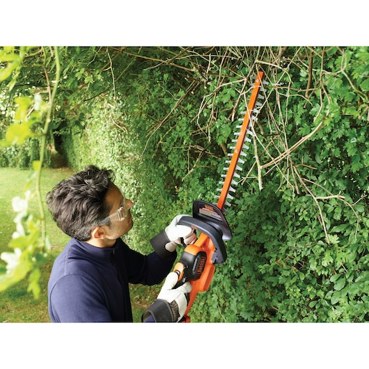 BLACK+DECKER GTC18504PC hedge trimmer with orange blade cutting bushes outdoors.