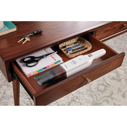 BLACK+DECKER HLVC315B11 handheld vacuum in a wooden desk drawer with scissors, notepad, and pens.