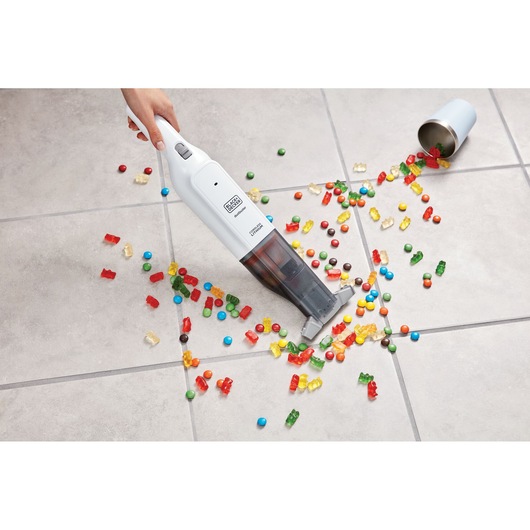 BLACKDECKER HLVC315J11 handheld vacuum cleaning colorful candy from tile floor, top angle.