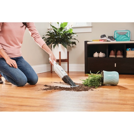 BLACKDECKER HLVC315J11 handheld vacuum cleaning soil from spilled plant on wooden floor.