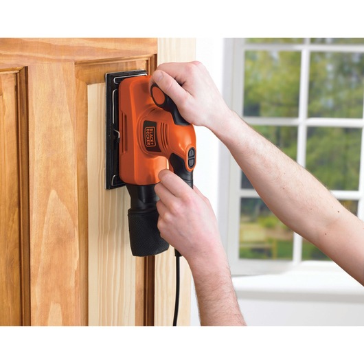 BLACKDECKER KA320EKA orange electric sander in use on a wooden door, close-up view.