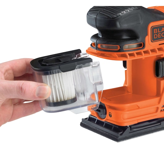 BLACK+DECKER KA330E sander with dust filter being removed, orange and black, close-up on white background.