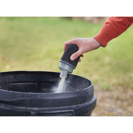 BLACKDECKER KA450 dust filter accessory in use, releasing dust into a black container outdoors.