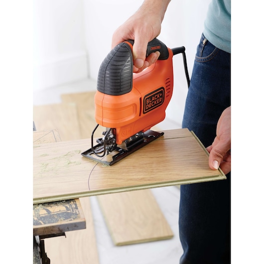 Photo of BLACKDECKER KS701EK jigsaw cutting wood panel, ergonomic orange and black design.