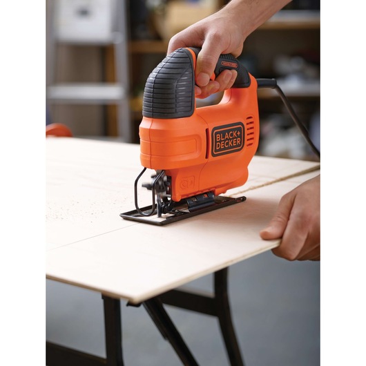 BLACKDECKER KS701EK orange jigsaw tool in use cutting wood on a workbench, close-up photography.