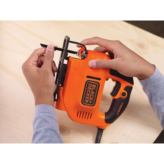 Photo of BLACK+DECKER KS701EK jigsaw in orange and black, being held and adjusted by two hands.