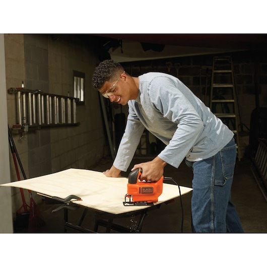 BLACKDECKER KS701E jigsaw cutting wood on workbench in workshop setting.