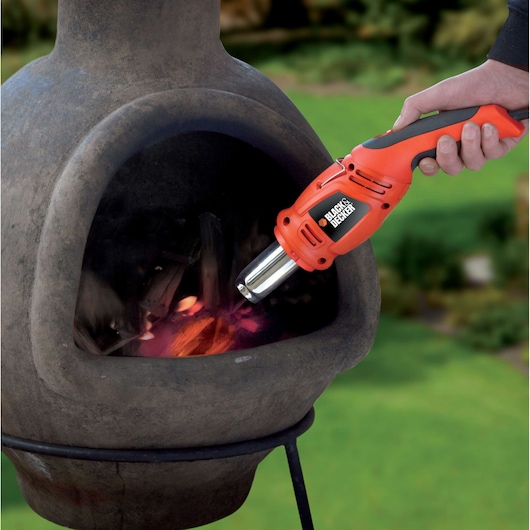 BLACKDECKER KX1692 heat gun used to ignite wood in outdoor fireplace, close-up view.