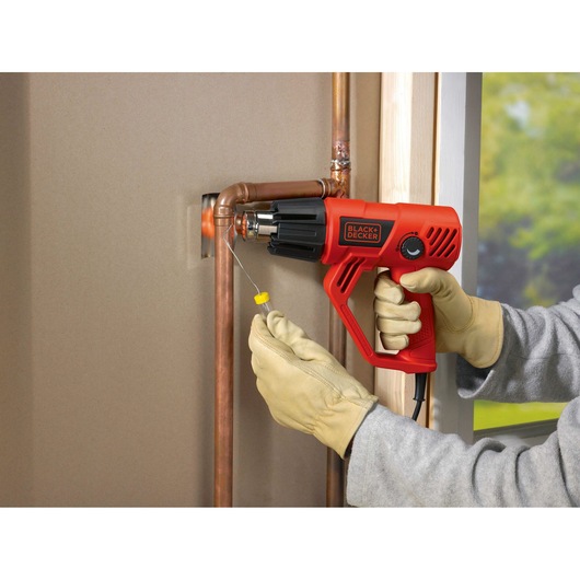 BLACKDECKER KX2001K heat gun used on copper pipes, person wearing gloves, indoor setting.