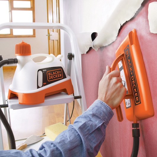 BLACK+DECKER KX3300T wallpaper steamer in use against wall, close-up of orange and white unit and steamer plate.