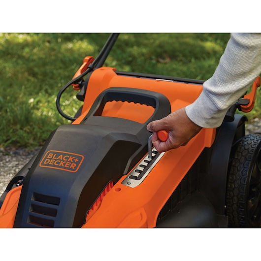 Photo of BLACK+DECKER LM2000 lawn mower height adjustment lever in use, orange and black housing visible.