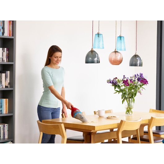 BLACKDECKER NVC115WAR handheld vacuum cleaning crumbs on dining table near flowers and mugs in kitchen.