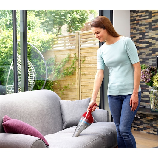 Photo of BLACKDECKER NVC115WAR handheld vacuum cleaning gray sofa indoors.