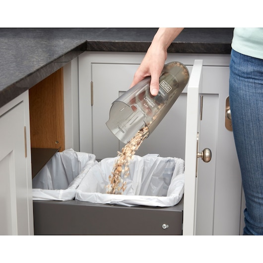 BLACKDECKER NVC115WA hand vacuum being emptied into kitchen trash bin, close-up view.
