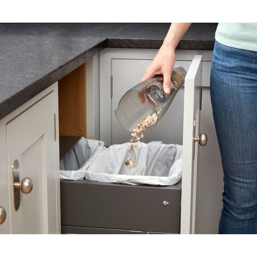 Photo of BLACKDECKER NVC215W handheld vacuum being emptied into a kitchen trash bin.