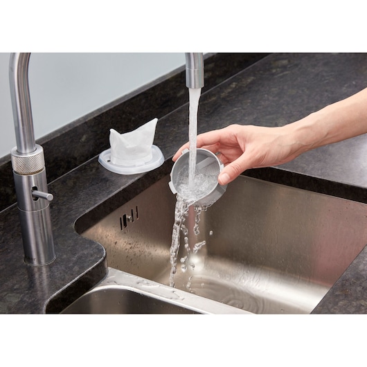 BLACKDECKER NVC215W vacuum filter being rinsed under running water over a kitchen sink.
