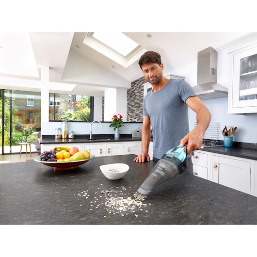 BLACKDECKER NVC220WBC handheld vacuum cleaning kitchen countertop with spilled oats visible.