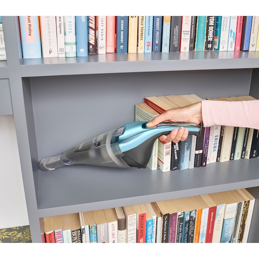 Photo of BLACKDECKER NVC220WBC handheld vacuum cleaning gray bookshelf near books.