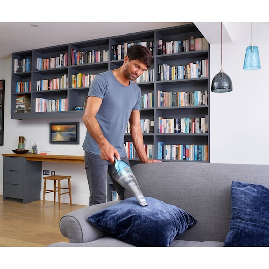 BLACKDECKER NVC220WBC handheld vacuum cleaner used on grey sofa with blue cushion in modern living room