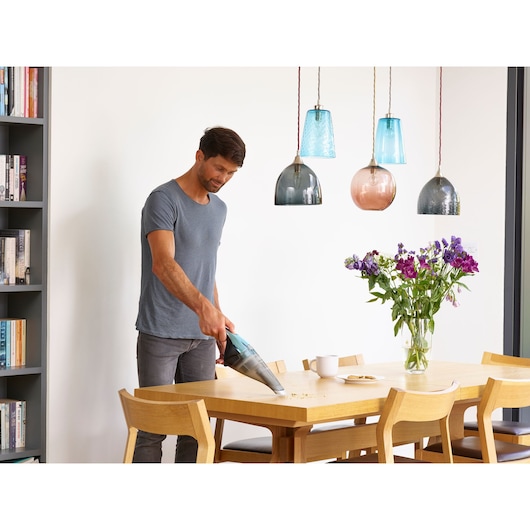 BLACK+DECKER NVC220WBC handheld vacuum cleaning crumbs from dining table in modern kitchen setting.