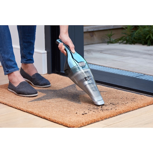 BLACKDECKER NVC220WBC handheld vacuum cleaning dirt on a doormat near a doorway.