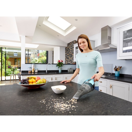 BLACKDECKER NVC220WBC handheld vacuum cleaning kitchen countertop with spilled oats near fruit bowl.