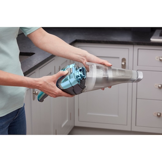 Person using BLACKDECKER NVC220WBC handheld vacuum cleaner in a kitchen.