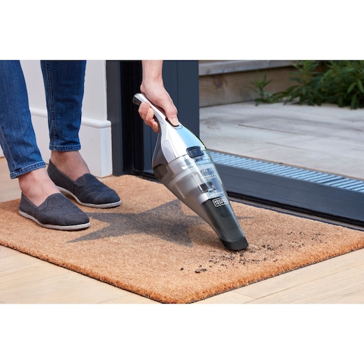 BLACK+DECKER NVC220WC handheld vacuum cleaning dirt from a brown doormat near a doorway.