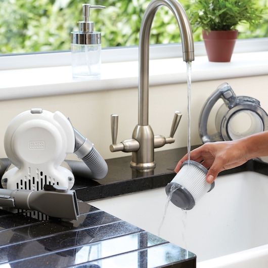 BLACKDECKER PD1020L handheld vacuum filter being rinsed under kitchen faucet, vacuum parts on counter.